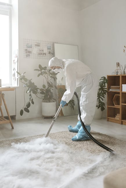A person performing surface cleaning with a vacuum cleaner on a dark carpeted floor in a professional setting, possibly a conference room or auditorium. The individual is bent over, focused on vacuuming, and is dressed in light-colored work attire. Behind them, there is a black wall with a grey radiator and a large white projection screen or panel above. The room features subdued lighting, highlighting the cleanliness and maintenance work being carried out, consistent with professional cleaning services offered by Haringey Carpet Cleaning. The scene emphasizes thorough carpet cleaning as part of deep cleaning and hygiene maintenance.
